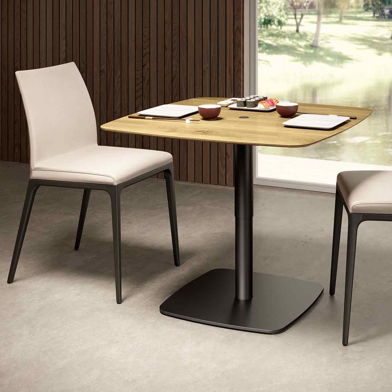 Ronald Schmitt – Triplex P430 bombiert | 90x90 cm, Tischplatte Wildeiche Natur, Bodenplatte Hochgefahrener Tisch mit an den Ecken abgerundeter Tischplatte aus hellem Holz auf schwarzer Bodenplatte. Milieubild mit Stühlen.